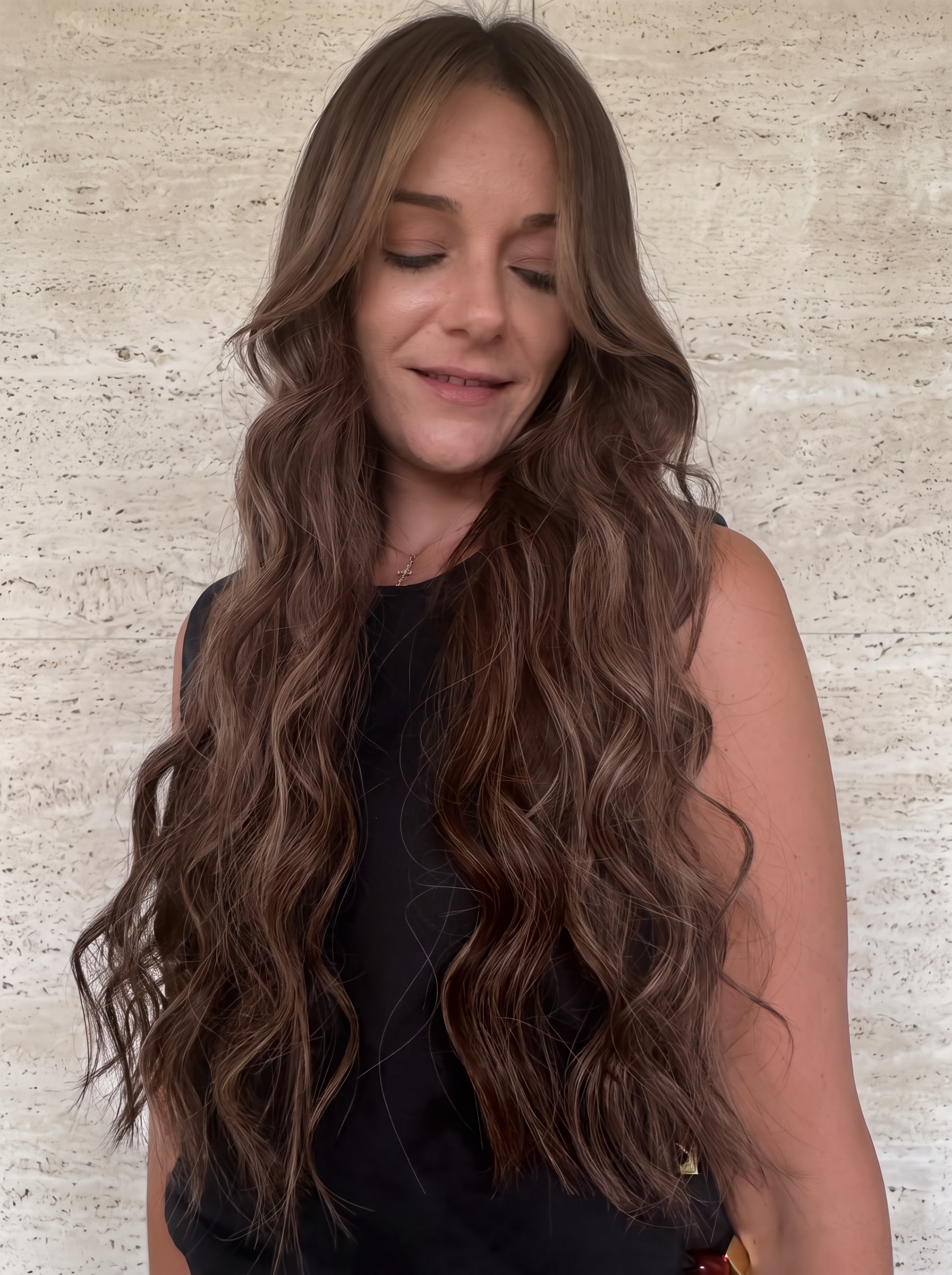 Long brunette waves viewed from the front against beige stone