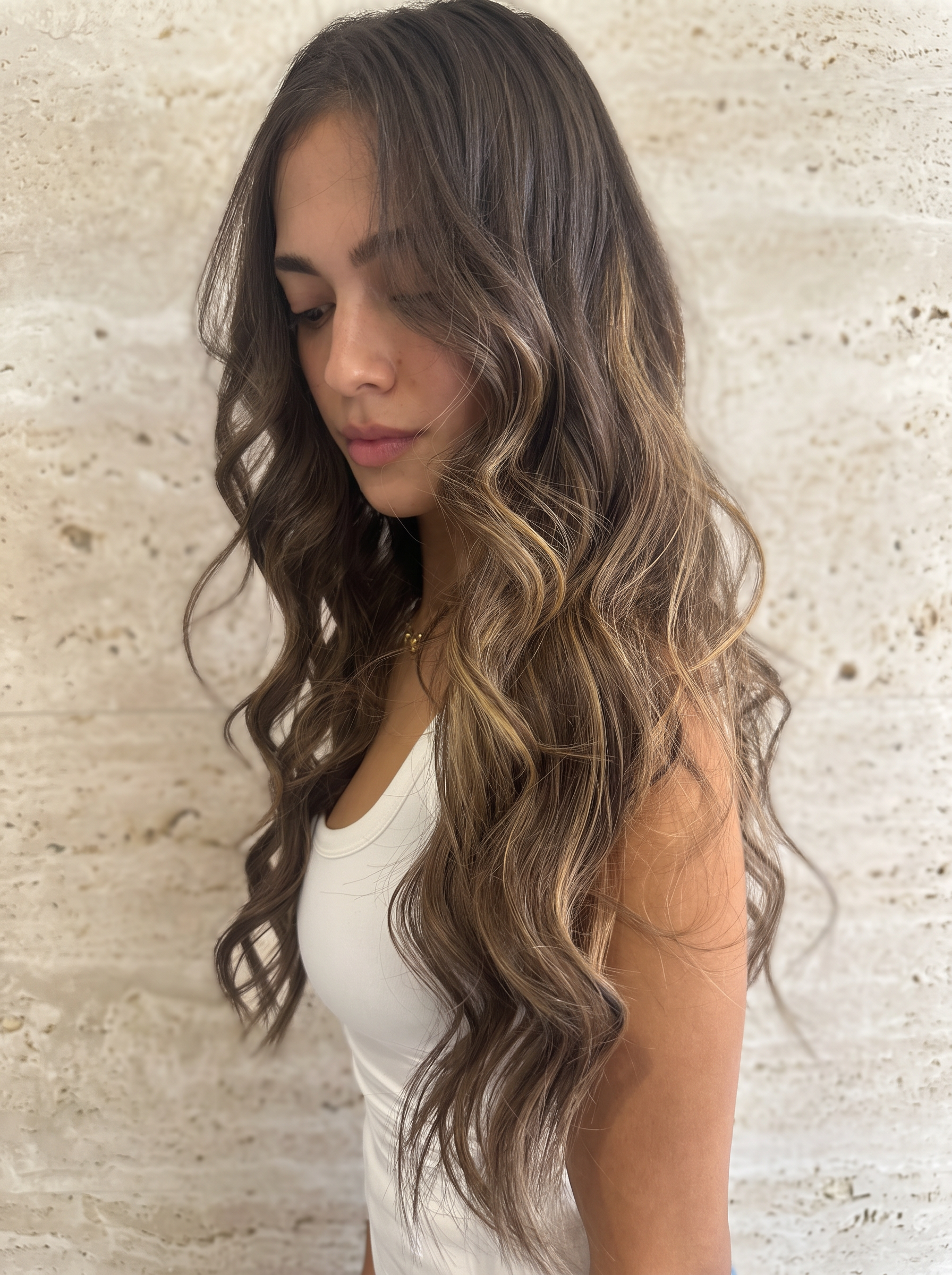 Dimensional brunette waves and face framing highlights against beige stone