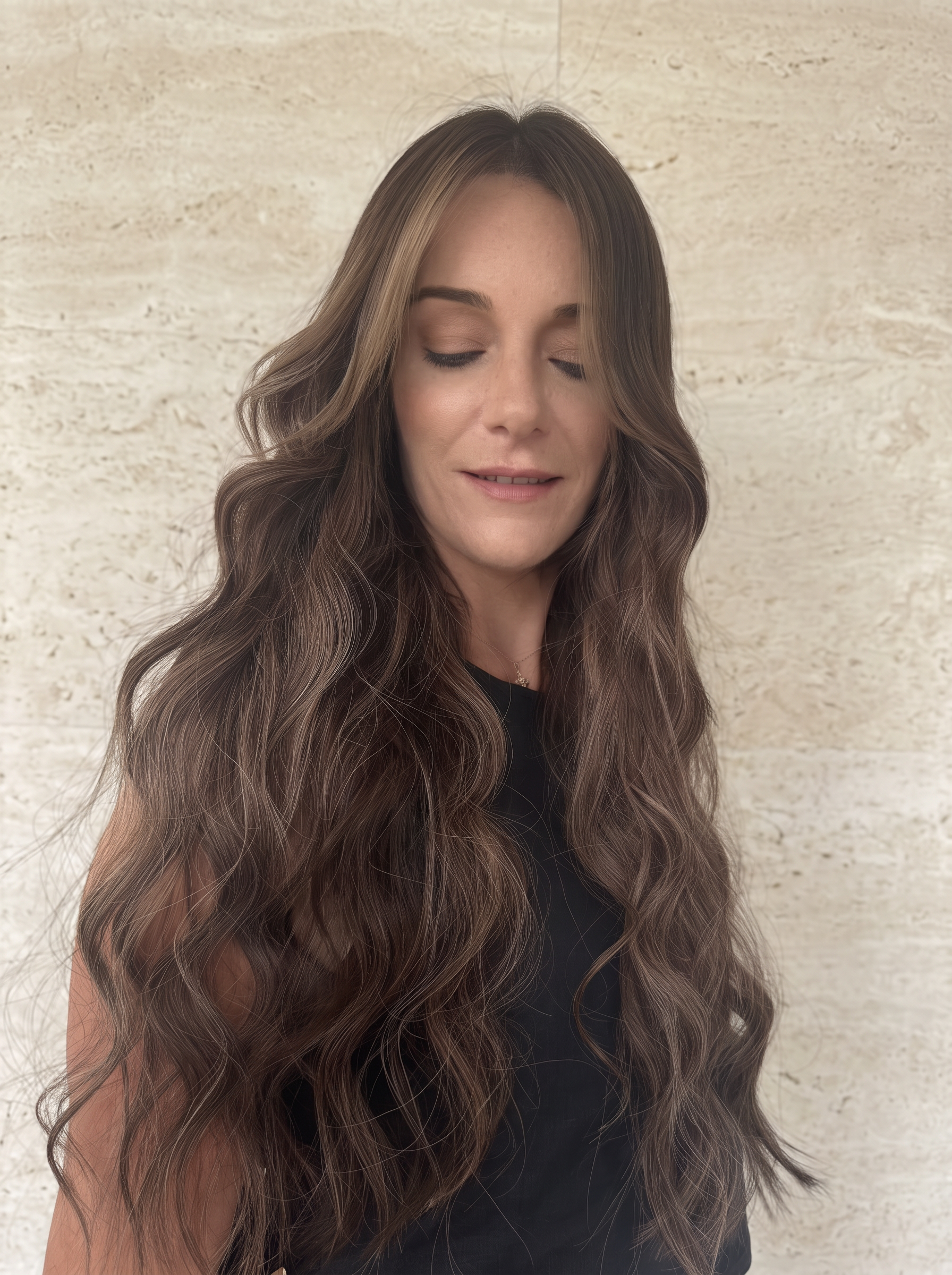 Soft flowing brunette waves with a centre part against beige stone
