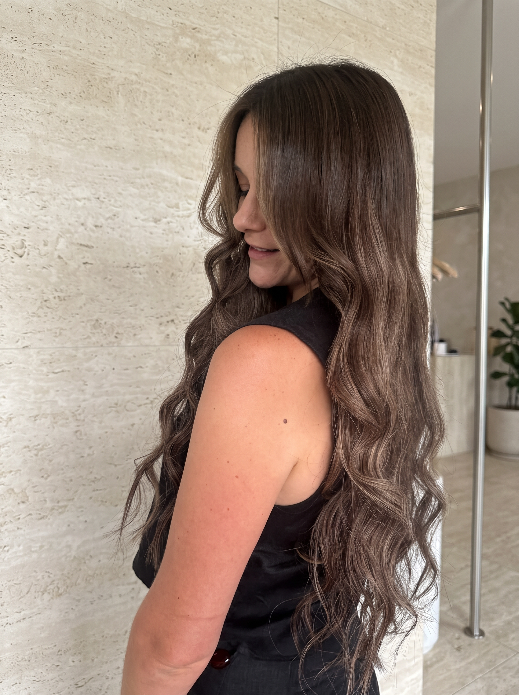 Long brunette waves viewed over the shoulder against beige stone